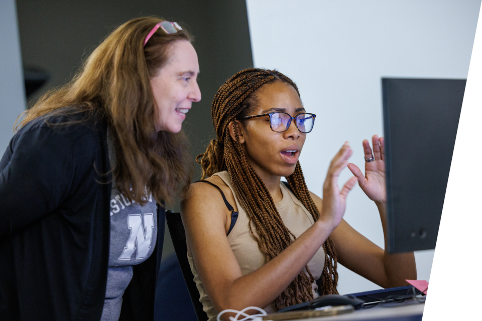 A professor and student look at a computer monitor.