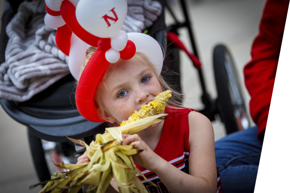 Young girl eating corn in a Nebraska balloon hat.